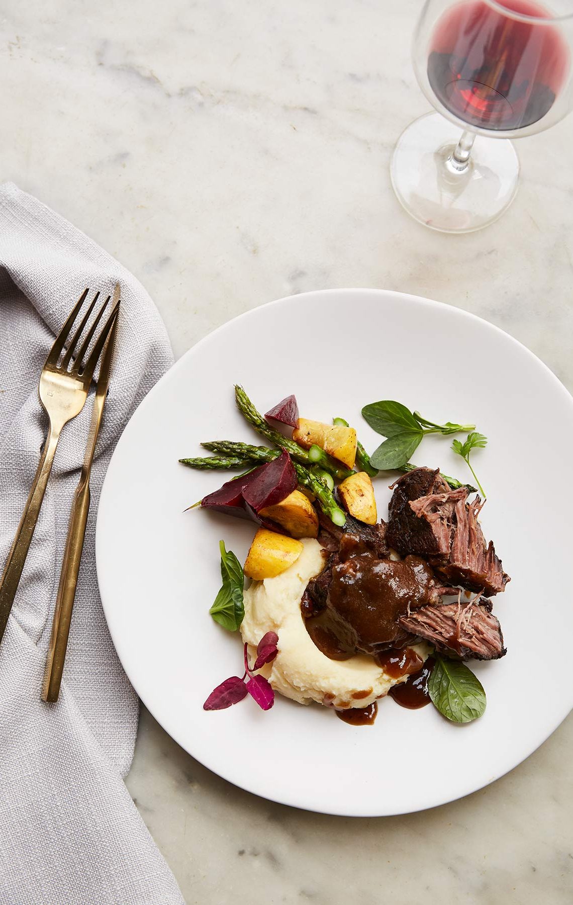 Short ribs with beets over mashed potatoes. White plate and gold flatware.