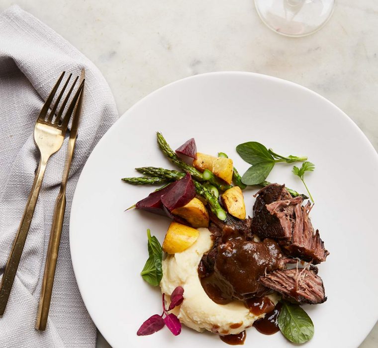 Short ribs with beets over mashed potatoes. White plate and gold flatware.
