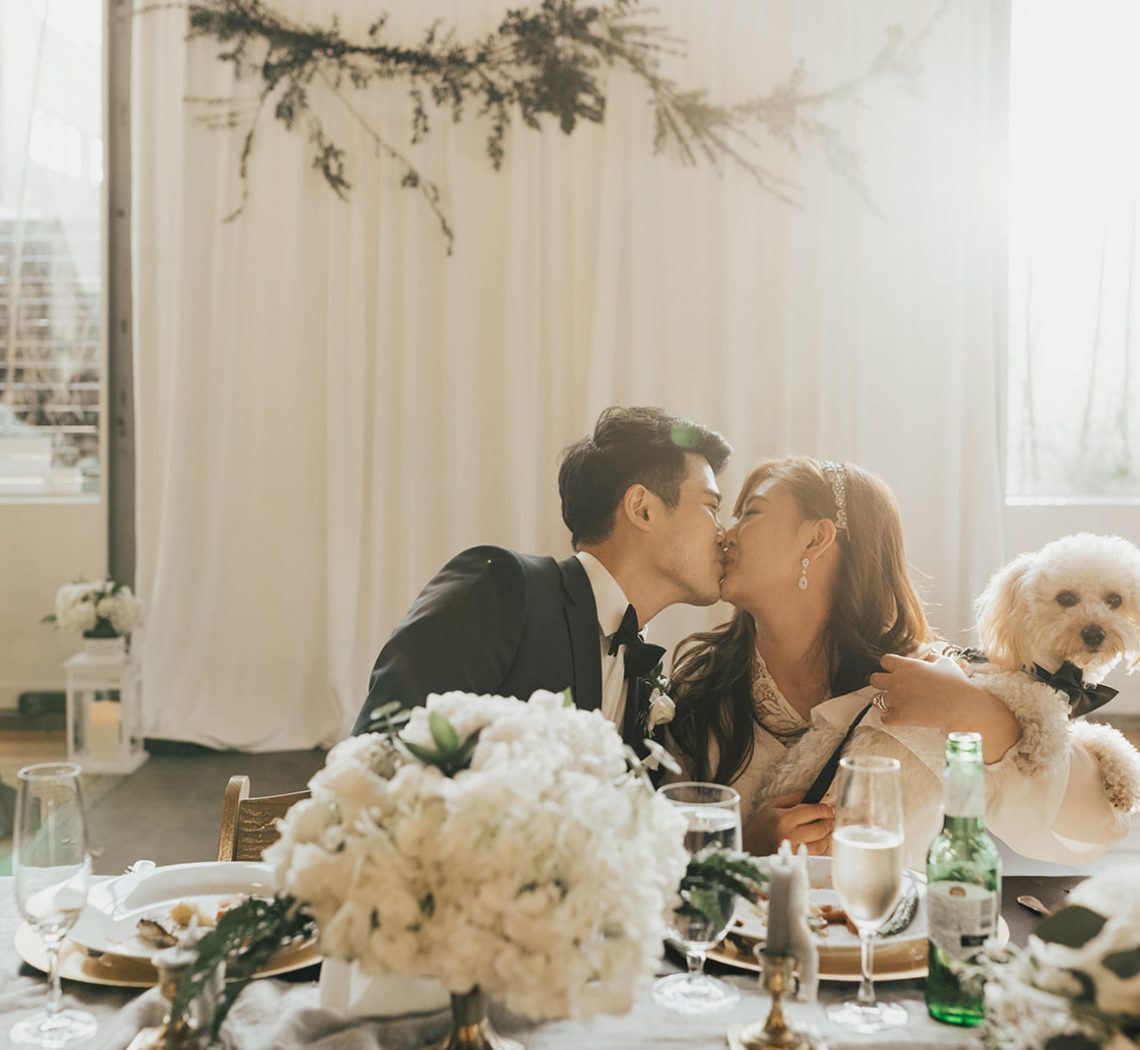 Newlywed couple kissing at wedding with their dog.
